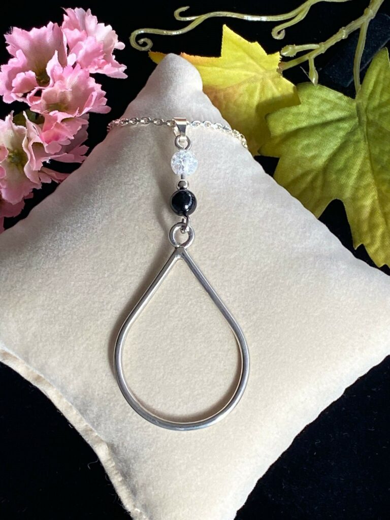 pendentif en forme de goutte surmonté de 2 perles une en tourmaline noire et l'autre en quartz craquelé blanc. représentation du yin et du yang
